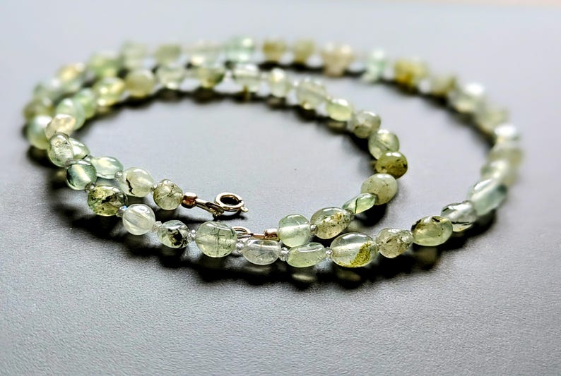 May include: A green and white gemstone necklace with a silver clasp. The necklace is made of oval-shaped beads.