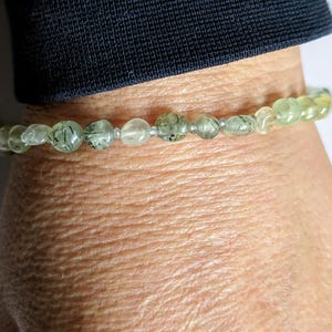 May include: A green and clear crystal bracelet with silver beads. The bracelet is on a person's wrist.