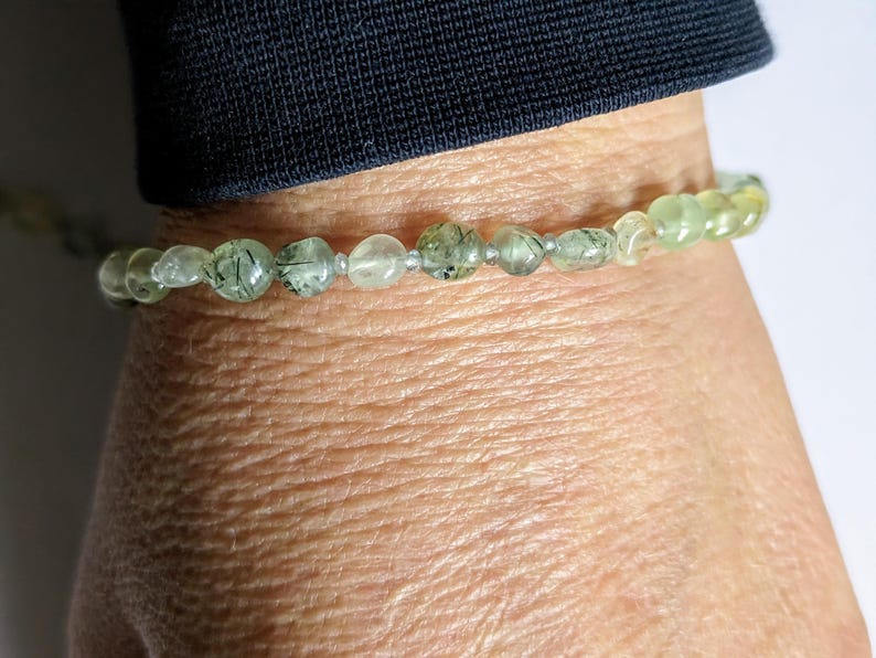 May include: A green and clear crystal bracelet with silver beads. The bracelet is on a person's wrist.