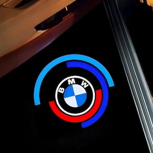 May include: A black surface displaying a BMW logo. The logo is a circular emblem in white and blue, with the letters "BMW", encircled by red and blue arcs.