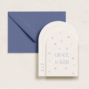 Puede incluir: Una tarjeta blanca con un diseño floral y el texto "GRACE and KALEB" en azul. La tarjeta tiene forma de arco y tiene un sobre azul.