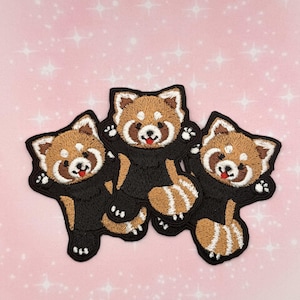 May include: Three embroidered patches of cartoon red pandas with brown and white fur, black bodies, and smiling faces. The patches are on a pink background with white sparkles.