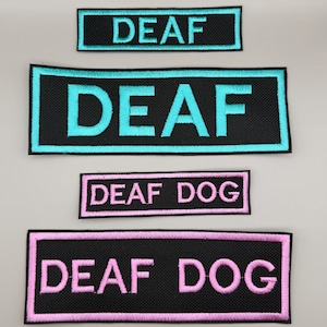 May include: Four rectangular embroidered patches with black backgrounds. Two patches feature the word DEAF in bright cyan thread with matching borders. Two patches feature the text DEAF DOG in light pink thread with matching borders.