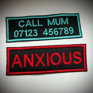 May include: Two rectangular embroidered patches with black fabric backgrounds. The top patch features teal text reading CALL MUM 07123 456789 with a teal border. The bottom patch features red text reading ANXIOUS with a red border.