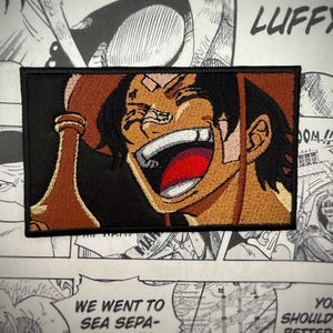 May include: Embroidered patch featuring a cartoon character with brown hair, a brown hat, and a wide, toothy grin. The character is holding a brown bottle in their right hand. The background is black. The text "DOM!!" is visible in the upper right corner of the patch.