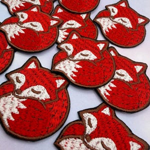 May include: Embroidered patches with a curled-up fox design. The patches have a red body, white chest, and brown outline. The fox is depicted sleeping with its eyes closed. Suitable for clothing or accessories.