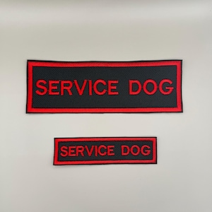 May include: Two rectangular embroidered patches featuring a black background with a red border and the text SERVICE DOG in red capital letters. The patches are identical in design, with one significantly larger than the other.