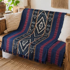 May include: A rectangular throw blanket featuring a deep blue base with a central vertical panel of white and dark blue diamond patterns. The blanket is accented by maroon vertical stripes and finished with a fringe along the bottom edge.