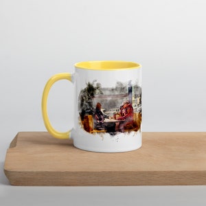 May include: A white ceramic mug with a yellow rim, featuring a watercolor illustration of two people sitting at a table in a diner. The illustration is in shades of brown, red, and yellow.