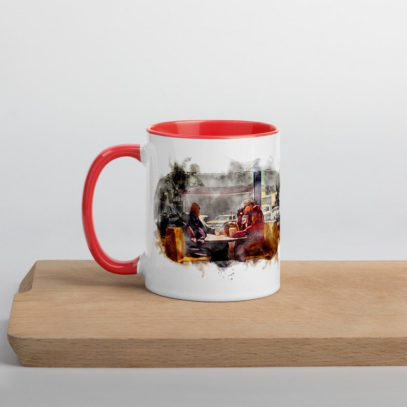 May include: A white ceramic mug with a red rim and handle. The mug features a watercolor illustration of two people sitting at a table in a diner.