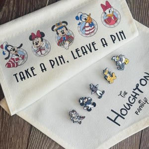 May include: Two off-white fabric panels with Disney character graphics and text. The top panel reads "TAKE A PIN, LEAVE A PIN" with character illustrations. Below are character pins, and the bottom panel has "The Houghton Family" text.