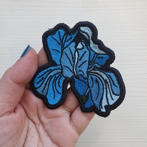 Puede incluir: Un parche de hierro azul bordado con una flor de iris.