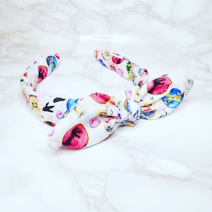 May include: White fabric headband with a bow, decorated with colourful illustrations of Easter eggs, bunnies, and other spring-themed designs. The headband is a stylish accessory for the spring season.