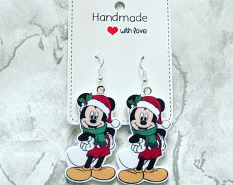 May include: A pair of dangle earrings featuring a Christmas-themed Mickey Mouse design. The earrings are made of silver metal and have a white background with a red and green Mickey Mouse wearing a Santa hat and scarf.
