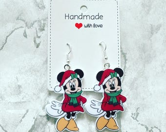 May include: A pair of silver dangle earrings featuring a Christmas-themed Minnie Mouse design. The earrings are handmade with love and feature a red dress, green scarf, and Santa hat.