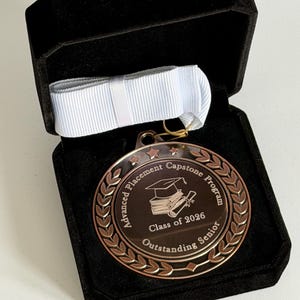 May include: A bronze medal, inscribed with "Advanced Placement Capstone Program", "Class of 2026 Outstanding Senior", and a laurel wreath design. Presented in a black velvet box with a white ribbon.