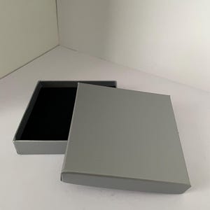 May include: A grey cardboard box with a black velvet interior. The box is open and the lid is lying next to it.