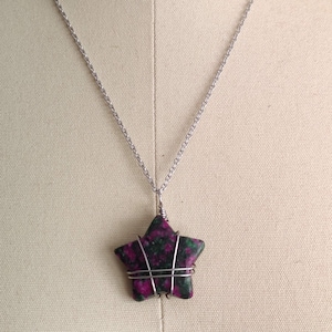May include: A silver chain necklace with a star-shaped pendant made of green and pink stone. The stone is wrapped in silver wire.