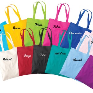 May include: A collection of 12 colourful tote bags with different embroidered text in French. The bags are arranged in a semi-circle, with the handles facing outwards. The colours of the bags include turquoise, yellow, green, fuchsia, blue, pink, red, black, white, teal, light blue, and purple.