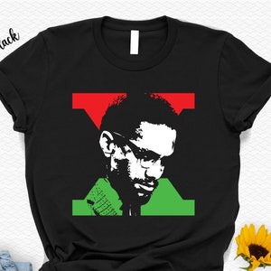 May include: Black t-shirt featuring a silhouette of Malcolm X in a red, green and black colour scheme.