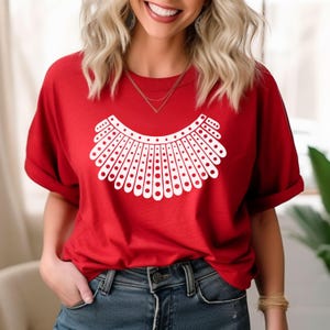 A woman wearing a red t-shirt with a white design on it, smiling and posing for the camera.