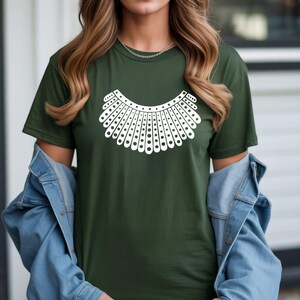 A woman wearing a green t-shirt with a white graphic design on it, standing in front of a building.