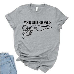 A gray t-shirt with a graphic design of a squid and the text "#SQUID GOALS" printed on it.