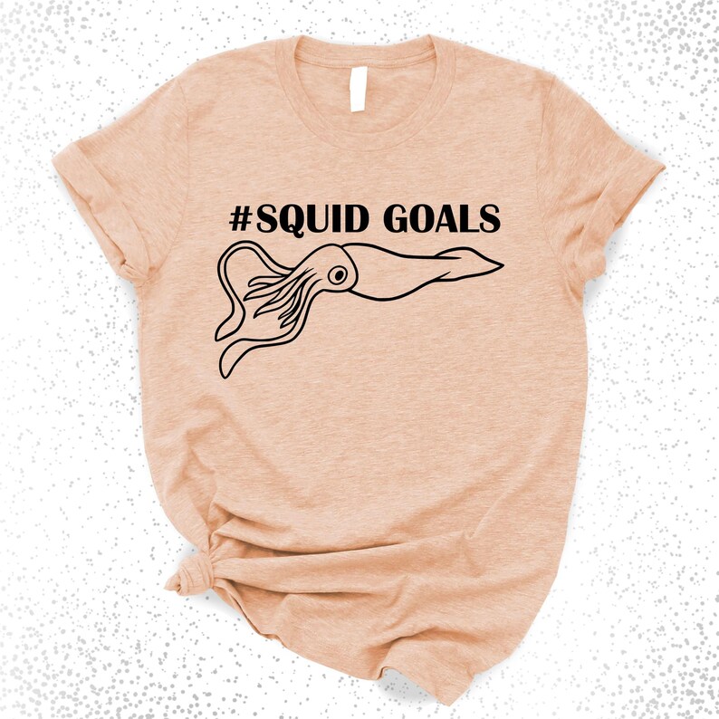 A peach-colored t-shirt with a graphic design featuring a squid and the text "#SQUID GOALS" printed on it.