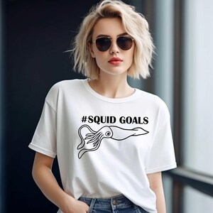 A woman wearing a white t-shirt with a graphic of an octopus and the text "#SQUID GOALS" printed on it.