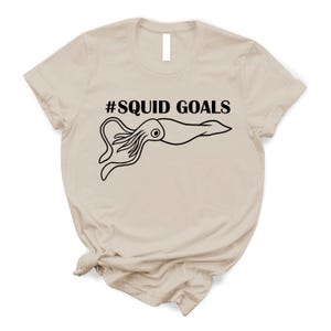 A beige t-shirt with a graphic design featuring a squid and the text "#SQUID GOALS" printed on it.