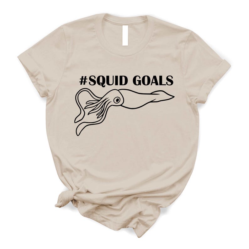 A beige t-shirt with a graphic design featuring a squid and the text "#SQUID GOALS" printed on it.