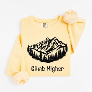 May include: A yellow sweatshirt with a black mountain range graphic and the text "Climb Higher".