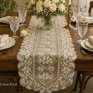 May include: A sheer table runner featuring intricate white and gold floral embroidery with a scalloped edge. The design includes a repeating diamond pattern filled with flower motifs and leaf borders, centered on a wooden dining table.