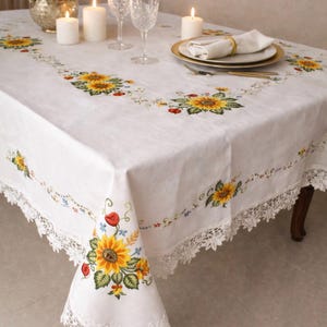 May include: White rectangular tablecloth with embroidered sunflowers, red poppies, and green leaves. The tablecloth has a delicate lace trim and is set with candles, glassware, and a floral centerpiece, creating an elegant dining setting.
