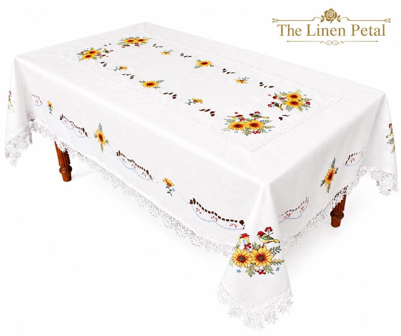 May include: White rectangular tablecloth with embroidered sunflowers and birds. The tablecloth has a lace trim and is set on a wooden table. The Linen Petal logo is in the upper right corner.