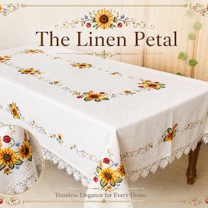 May include: A white rectangular tablecloth featuring embroidered sunflowers and a lace trim. The text "The Linen Petal" is displayed at the top, with "Timeless Elegance for Every Home" at the bottom. The tablecloth is draped over a wooden table.