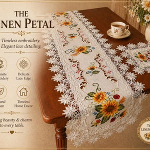 May include: A white linen table runner with embroidered sunflowers and delicate lace edging. The runner is on a dark wooden table, with a matching placemat and a cup of tea. The text on the image says "The Linen Petal".