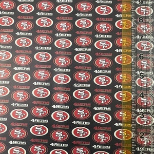 May include: Black fabric with a repeating pattern of the San Francisco 49ers logo in red and white. The logo features the letters "SF" inside an oval. The word "49ERS" is above and below the logo.