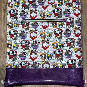 May include: A white zippered pouch with a purple bottom. The pouch is decorated with a repeating pattern of Jack Skellington and Sally from The Nightmare Before Christmas characters holding coffee cups and cupcakes.