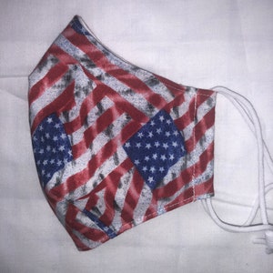 May include: A face mask with a red, white, and blue American flag pattern. The mask is made of fabric and has white elastic ear loops.