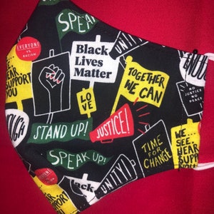 May include: Black and yellow face mask with a variety of protest slogans, including "Black Lives Matter", "Stand Up!" and "Speak Up!"