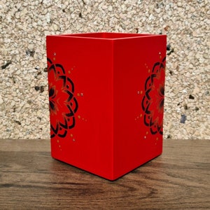 May include: Red square-shaped pencil holder with a black and gold mandala design.