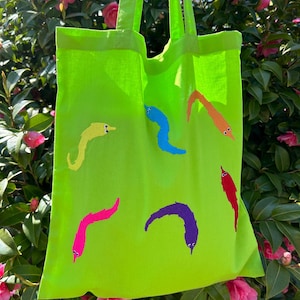 May include: A bright green tote bag featuring colourful worm illustrations. The worms are in various colours, including yellow, blue, purple, pink, orange, and red. Each worm has a simple smiling face.