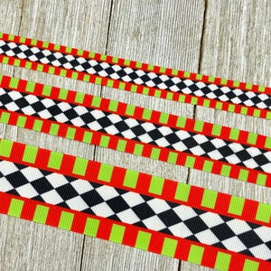 Puede incluir: Tres cintas decorativas con un patrón repetitivo de diamantes negros y blancos, rectángulos rojos y rectángulos verdes. Las cintas están dispuestas en diagonal sobre un fondo de madera.