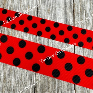 May include: Red grosgrain ribbon with black polka dots. The ribbon is on a wooden surface.