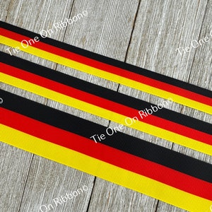 May include: Black, yellow, and red ribbon with the colors arranged in the order of the German flag. The ribbon is on a wood background. The text "Tie One On Ribbons" is visible in the image.