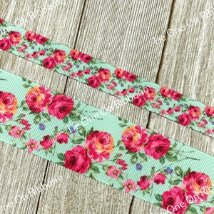 Puede incluir: Primer plano de una cinta azul claro con estampado floral con rosas rosas y naranjas. La cinta est&aacute; sobre una superficie de madera.