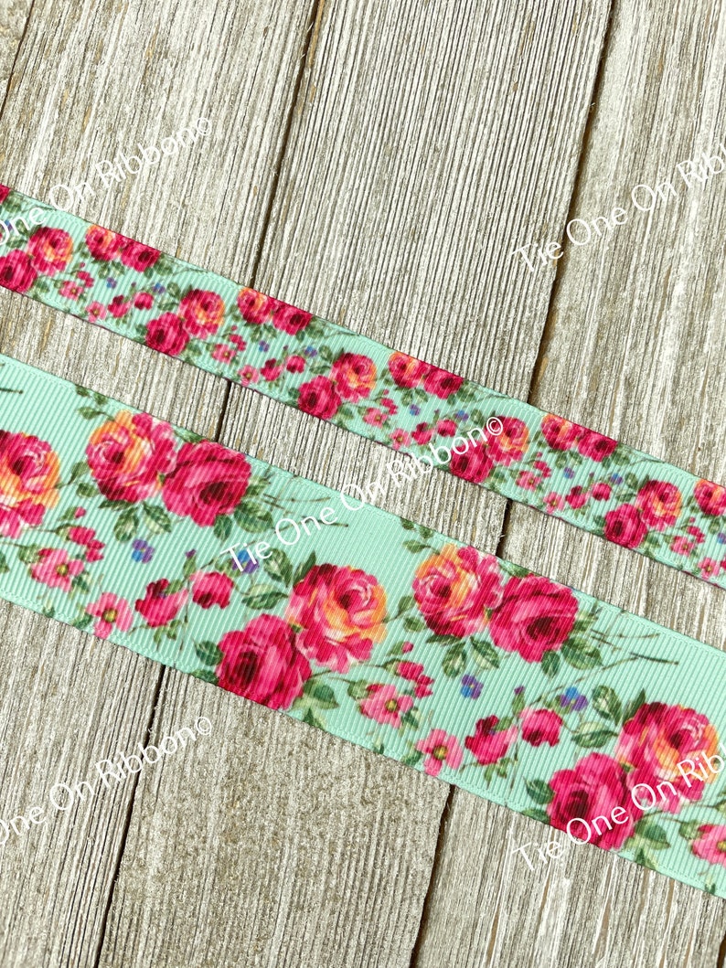 Puede incluir: Primer plano de una cinta azul claro con estampado floral con rosas rosas y naranjas. La cinta est&aacute; sobre una superficie de madera.