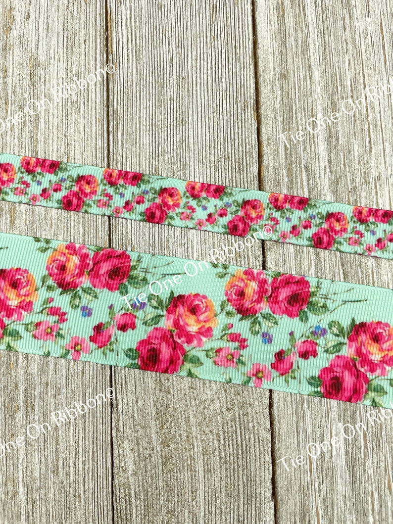 Puede incluir: Primer plano de una cinta azul claro con estampado floral con rosas rosas y naranjas. La cinta est&aacute; sobre una superficie de madera.