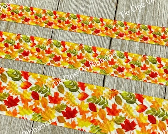 May include: A white ribbon with a colorful autumn leaf pattern. The ribbon features red, orange, yellow, and green leaves. The ribbon is perfect for crafting, decorating, and adding a touch of fall to your projects.